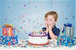 Kleiner Junge mit Geburtstagsgeschenke und machen einen Wunsch vor dem Ausblasen der Kerzen auf der Geburtstagstorte