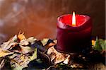 Lit candle sitting in dried leaves