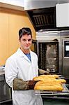 Happy baker showing his baguettes to the camera standing in his kitchen