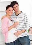 Portrait of a merry pregnant woman holding a glass of milk and of her husband touching her belly at home