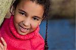 Portrait photograph of a beautiful young smiling happy mixed race interracial African American girl, shot outside in a park with a lake in the background.
