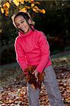 Photograph of a beautiful young smiling happy mixed race interracial African American girl playing with leaves under the golden leaves of a tree during the Fall or Autumn