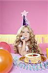 bored little blond girl in a birthday party with cake and candle on pink background