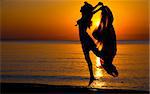 Silhouette of a girl jump down the beach at sunset. Natural light and dark. Artistic colors added. Horizontal photo