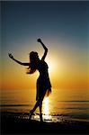 Girl dances on the beach at sunset. Natural light and dark. Artistic colors added. Vertical photo