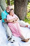 Romantic senior couple relaxes together outdoors under the trees.