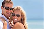 A sexy and attractive man and woman couple smiling and happy wearing sunglasses in sunshine at the beach