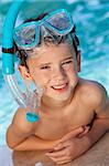 A happy young boy child relaxing on the side of a swimming pool wearing blue goggles and snorkel