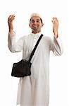 Ethnic mixed race man wearing white embroidered robe  and topi hat and carrying black shoulder bag and arms raised in praise or joy