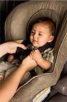 Smiling biracial Asian Filipino kid sitting in car seat while parent hands buckle him up