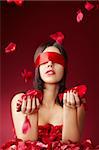 Charming girls blindfold with falling petals of roses on a red background