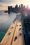 Busy traffic in New York City Manhattan with Brooklyn Bridge across Hudson River at sunset.