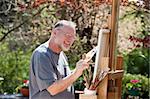 Man paints on an easel in a pleasant outdoor setting.