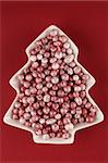 White bowl in the shape of Christmas tree full of little polystyrene Christmas pellets on red background.
