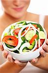 A close-up of a fresh vegetable salad with a pretty woman holding it in the background