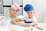 Happy brother and sister preparing a dough standing in the kitchen and looking at the camera