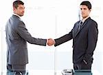 Two charismatic businessmen shaking hands standing in the office at work