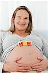Adorable blond woman with mom letters on her belly and smiling at the camera