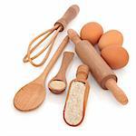 Baking equipment and products, with wholegrain flour, yeast and eggs, with rustic natural wooden spoons, scoop, whisk and rolling pin, isolated over white background.
