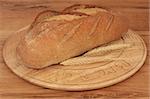 Rye bread loaf with wheat on a carved rustic wooden board against oak wood background.