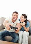 Cheerful woman encouraging her boyfriend playing video game at home