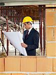 caucasian male architect holding blueprints near brick wall. Vertical shape, waist up, side view, copy space