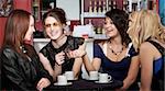 Four female students teasing one another over coffee at a cafe