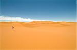 Woman walking alone among the sand dunes of the Sahara desert. Best of Morocco.