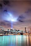 Remember September 11. New York City Manhattan panorama view with Brooklyn Bridge at night with office building skyscrapers skyline illuminated over Hudson River and two light beam in memory of September 11.
