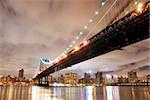 New York City Manhattan Bridge with city skyline at night illuminated over Hudson River.