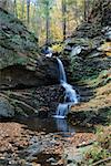 Waterfall in mountain with Autumn foliage and woods over rocks.