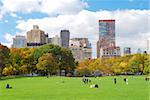 New York City Manhattan skyline panorama viewed from Central Park with cloud and blue sky and people in lawn.