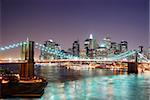 New York City Brooklyn Bridge and Manhattan skyline with skyscrapers over Hudson River illuminated with lights at dusk after sunset.