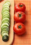Red-ripe tomatoes and slices of cucumber on kitchen board