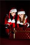 two woman in Santa costume opening christmas gift. on black .