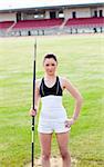 confident athletic woman ready to throw a javelin standing in a stadium looking at the camera