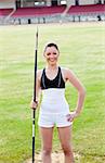 joyful sporty woman holding a javelin standing in a stadium and smiling at the camera