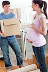 cute pregnant wife looking at her husband holding box standing in their new kitchen during removal