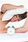 Man woken up by his alarm clock and putting pillow on his head