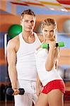 Girl and the man with dumbbells in hands in sports club