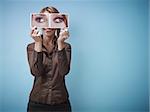 mid adult business woman holding photo of her eyes looking at different sides on blue background. Horizontal shape, front view, waist up, copy space