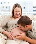 Proud man kissing the belly of his pregnant girlfriend sitting in the sofa in the living room