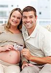 Proud couple of future parents holding an echography sitting on the sofa