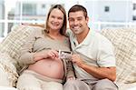 Cheerful couple of future parents holding an echography sitting on the sofa