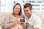 Beautiful pregnant woman showing her echography to her husband at home