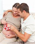 Cute man playing with baby shoes on his wife's belly at home