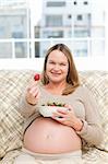 Futur mom with a bowl of strawberries sitting on the sofa at home