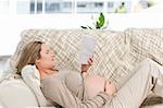 Concentrated pregnant woman reading a book lying on the couch at home