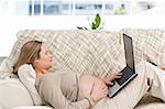 Smiling pregnant woman using her laptop lying on the sofa at home