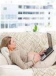 Relaxed pregnant woman using her laptop on the sofa of her living room